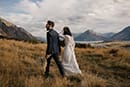 bride and groom walking in the middle of the mountains while the cold breeze pass by them- New Zealand Elopements